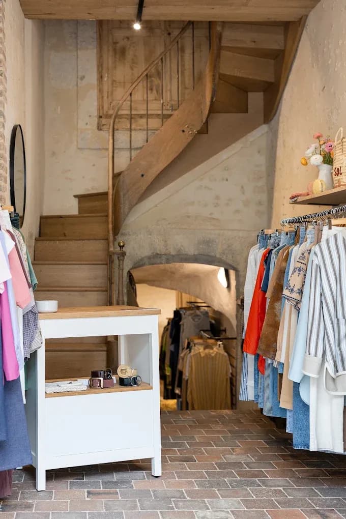 L'intérieur de la boutique : escalier en bois, portants de vêtements et sol en briques